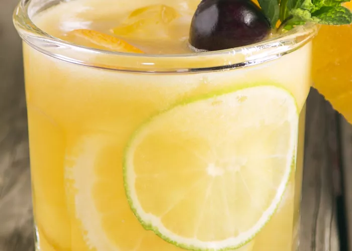 Glass of Sparkling Cherry Sangria garnished with orange wedge, lime slices, mint leaves and cherry
