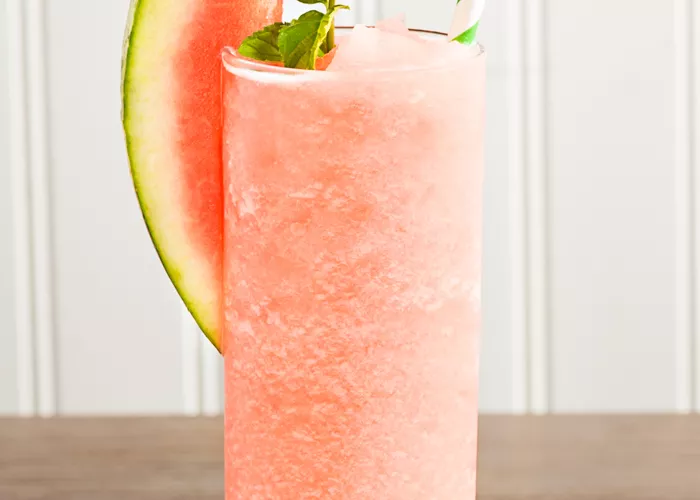 Glass of Downward Facing Daiquiri garnished with watermelon slice, mint leaves and a straws