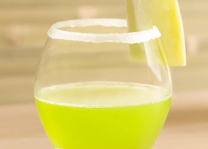 A glass with a emerald daiquiri and a slice of apple on top