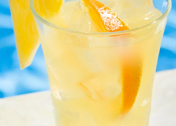 A glass of Endless Summer Punch garnished with ice cubes, an orange slice, and a pineapple slice on the rim