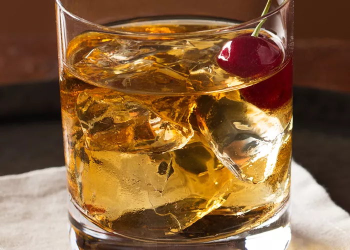 Glass of Buttershots® Old Fashioned garnished with cherry on white cloth