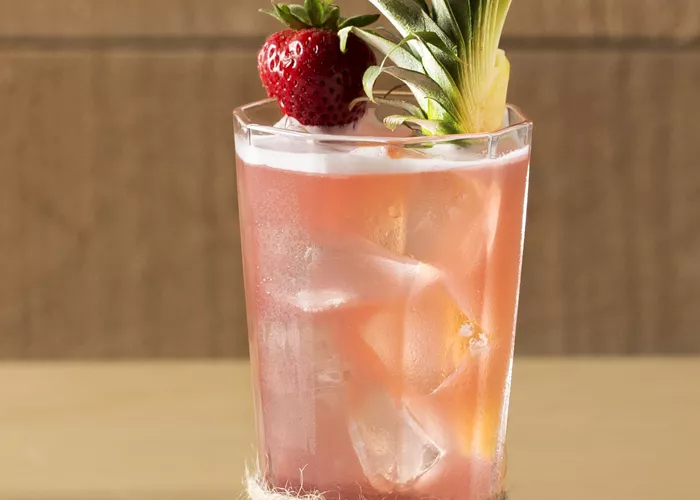Glass of Bay Breeze garnished with pineapple leaves and strawberry