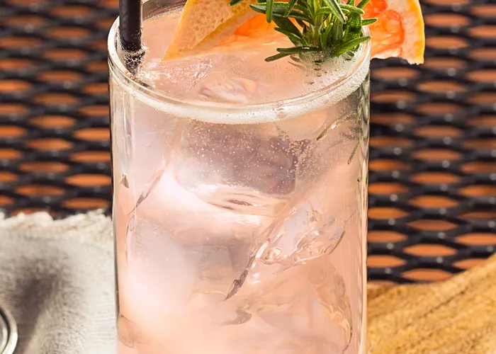 Glass of Paloma garnished with grapefruit wedge, rosemary sprig and straw