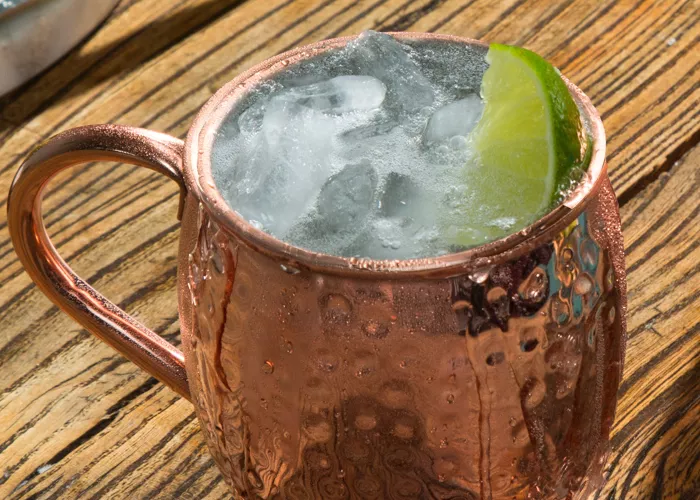 A copper cup of Bruxo® Mezcal Mule garnished with Lime Wedge