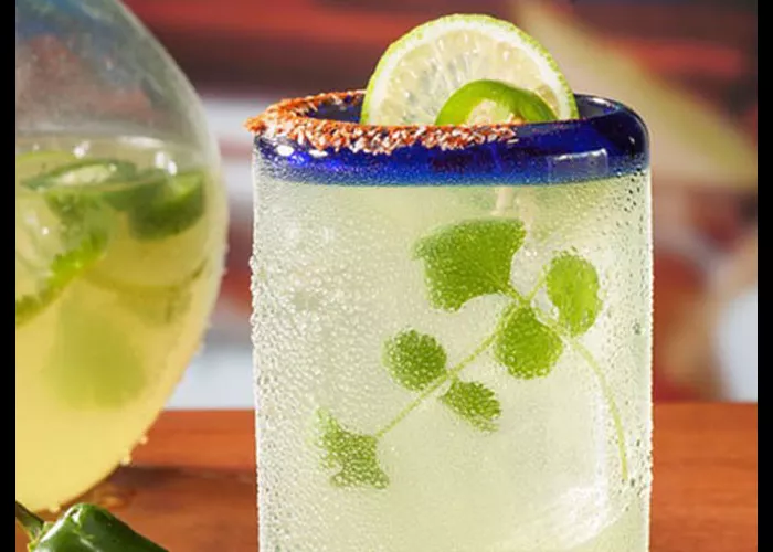 "A glass of Sauza® Cilantro Jalapeno Margarita garnished with  lemon  slice, jalapeno slice  and fresh cilantro on the rim of glass"