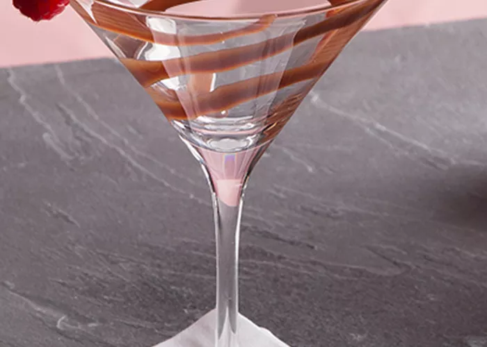 A Glass garnished with chocolate sauce and a Raspberry on rim placed on a white cloth