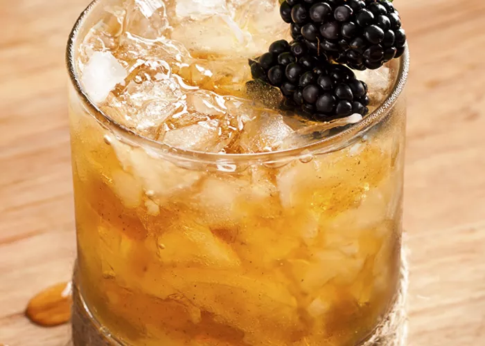 Glass of Hats Off Julep with crushed Ice, garnished with blackberries and mint leaves.