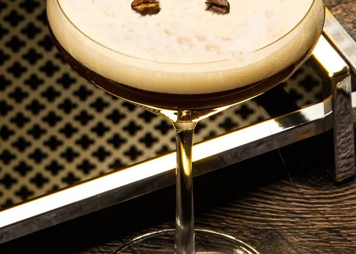A glass of Espresso Martini garnished with coffee beans along with the tray on the table .
