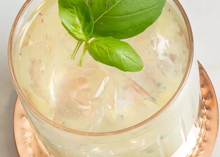 A glass of Gin Basil Smash garnished with mint leaves on a copper coaster 