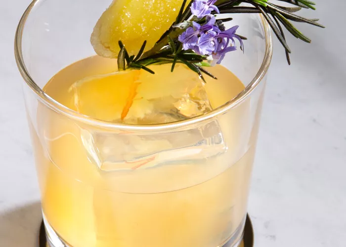 A glass of Ginger Buck  garnished with Sprig of Rosemary and Candied Ginger