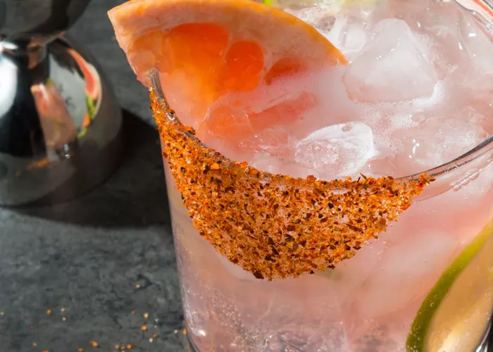 A glass of Hornitos® Paloma garnished with Grapefruit Wedge, Salt and Spice Rim and a chopped lemon