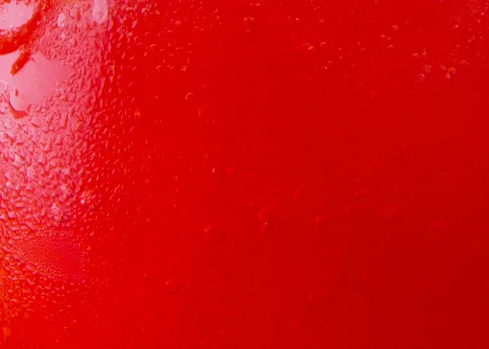 A snifter glass of Sunset Daiquiri placed on a coaster  and jute mat, garnished with cherry, lemon slice, lemon peel with straws inside.