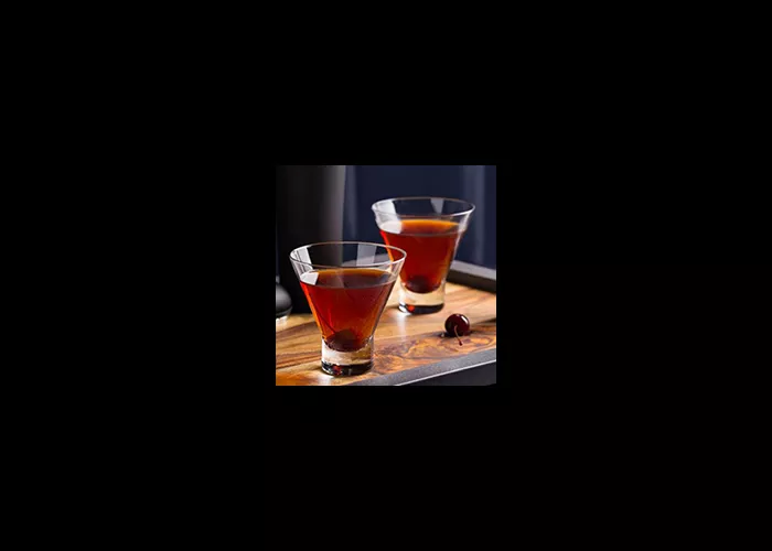 Two glasses of Jim Beam Black Manhattan garnished with a cherry in each, alongside a cherry on a wooden tray.