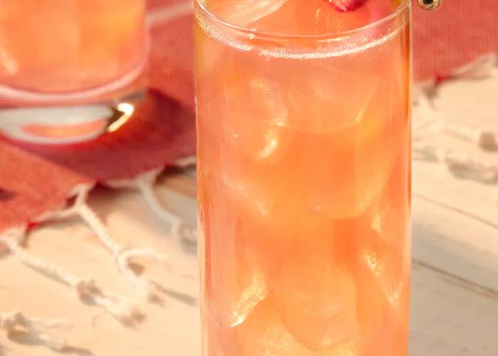 A glass of Kentucky Buck with strawsberry and lemon garnishes, placed on a wooden table next to an identical glass.