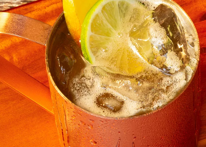 Two copper cups full of Kentucky Mule garnished with mango and sweet lemon  placed on a wooden frame