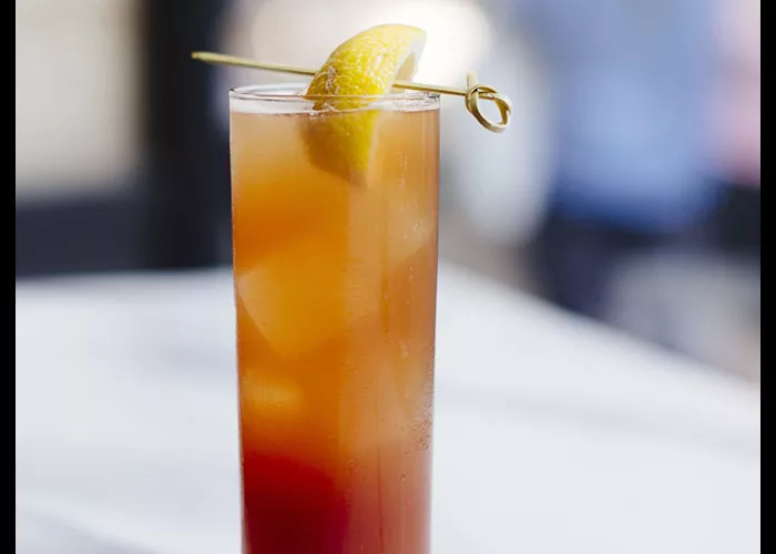 A glass of Laphroaig® Back Yard Collins, garnished with ice cubes and a lemon slice pierced with a toothpick on the rim of the glass