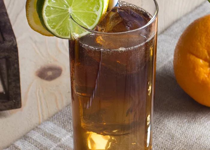 glasses of Long Island Iced Tea with a straws, garnished with a lime and lemon wheel on a mat.