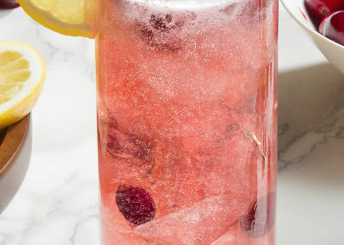 A glass of Maker's Mark® Merry Berry Buck garnished with Cranberries and lemons