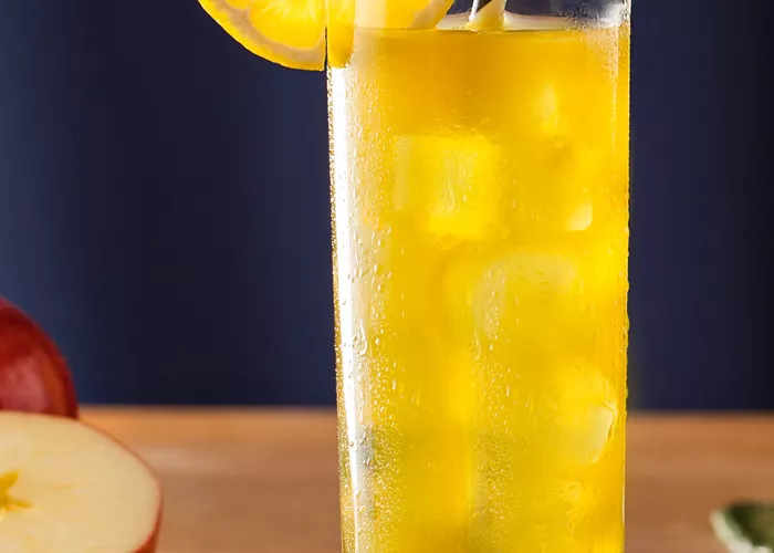 Two glasses of Midori® Cider with strawss on coasters, garnished with lemon wheels. Nearby, there is one and half apple.