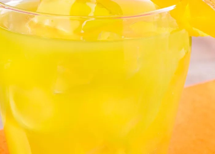 Glass of Pina Punch with ice, garnished with a mango and pineapple slice on an orange napkin. 