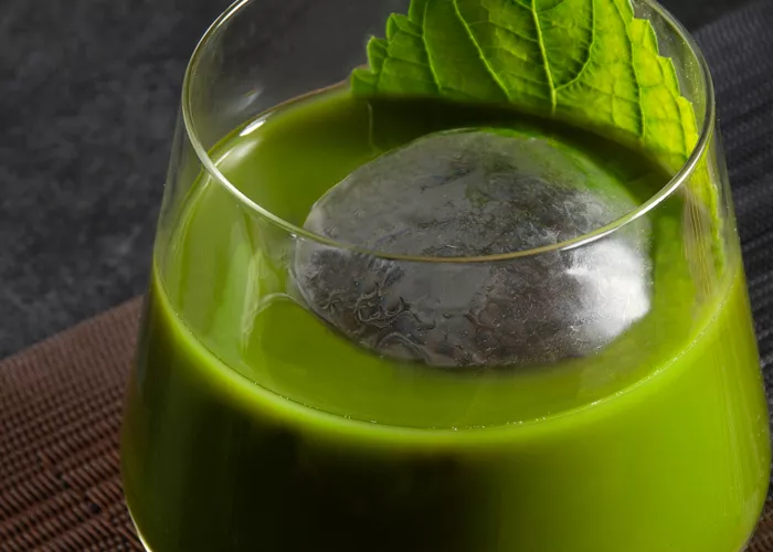 A glass of Tea' New Fashioned garnished with Fresh Shiso Leaf along 