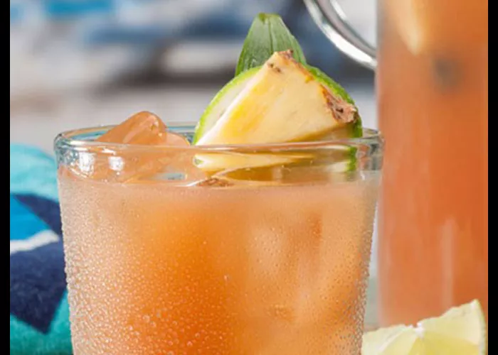 A glass of Pina Punch garnished with ice cubes, lemon slice and pineapple slice 
