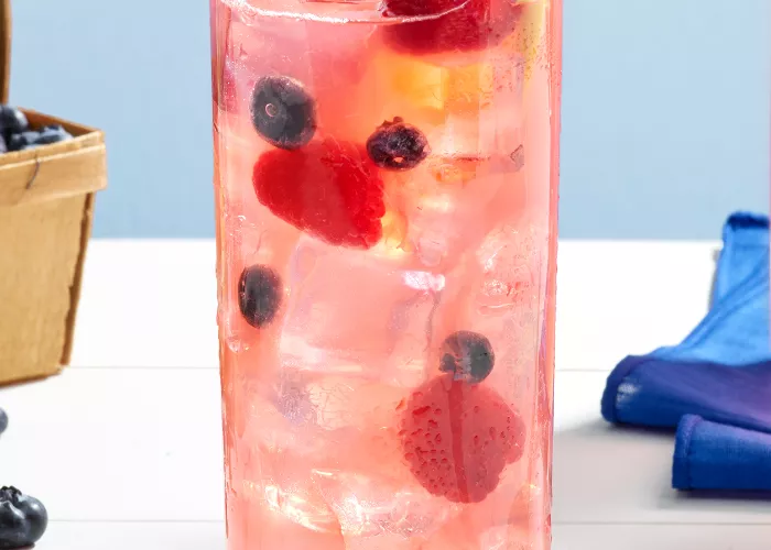 A glass of Pinnacle® Raspberry Lemonade garnished with Raspberries, Blueberries and Lemon Wheel