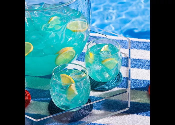 A tray with two glasses and a summer fish bowl containing a Ice-cold drink garnished with lemon.