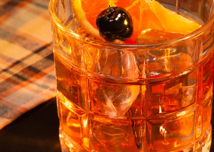 A  glass of Smoked Maple Old Fashioned garnished with Orange Slice and Cherries 
