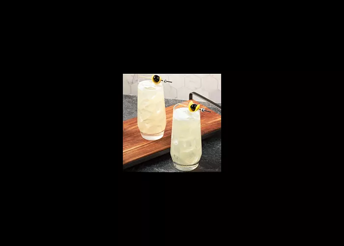 Two glasses of Tokyo Collins garnished with lemon peel and black cherries on a wooden try on the kitchen slab