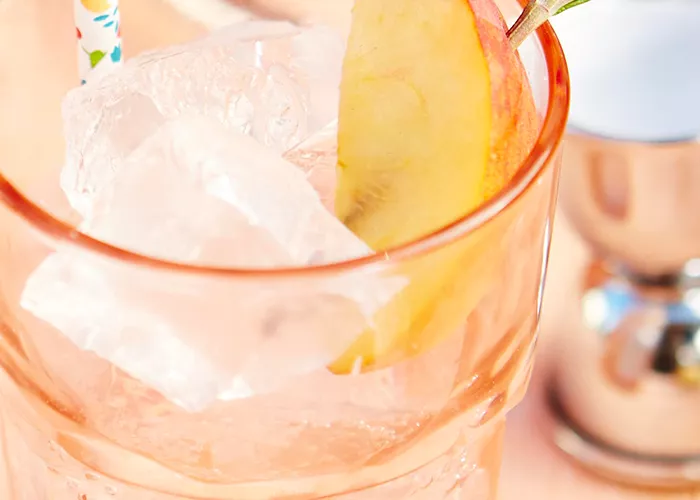 Glass of Peachy Keen garnished with peach slice and rosemerry with a straw