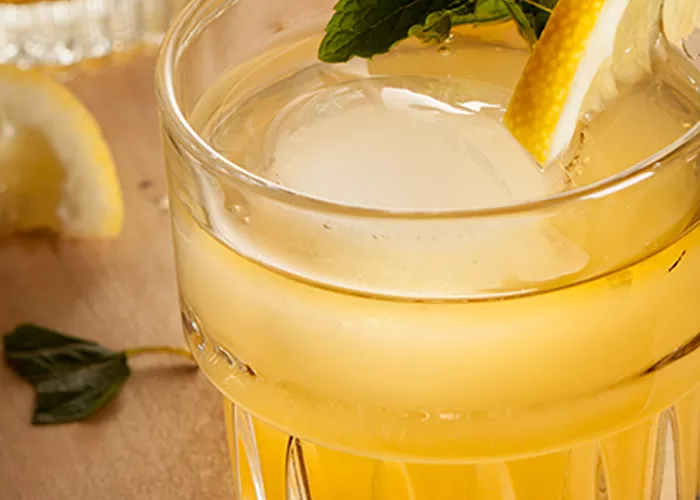 A glass of Cruzan® 9 Tea garnished with lemon wedge and mint leaves with some of them fallen alongside.