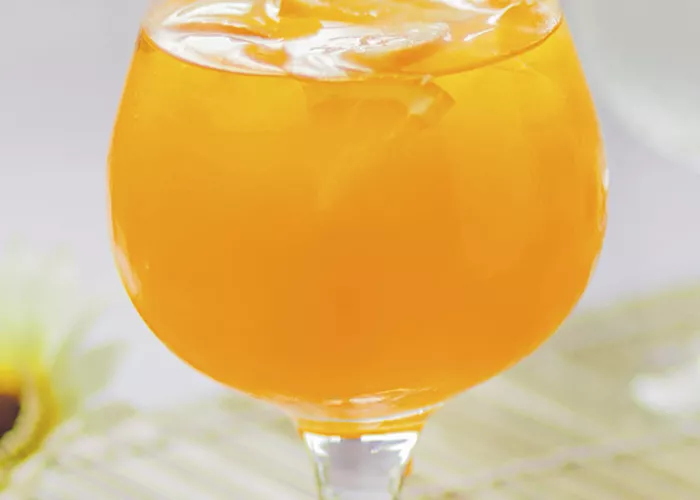 A glass of Key Lime Sparkler, garnished with a slice of orange peel. Along with half orange placed besides it.