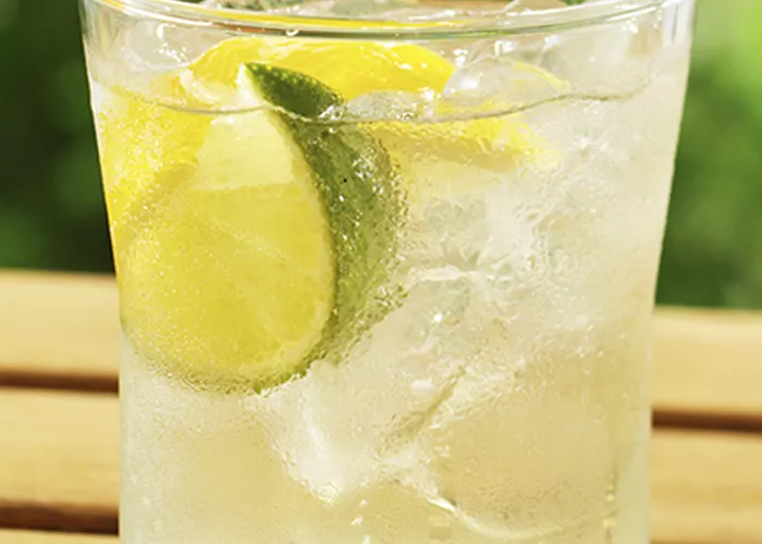 A glass of Light and Tonic placed on wooden table, garnished with a lime wedge.