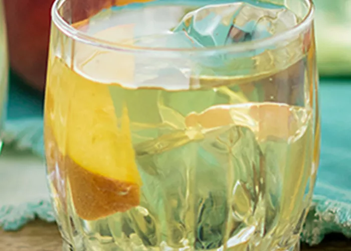 A pitcher of Paradise Punch placed with two glasses containing lemon juice and honey syrup  with wood honey dipper stick placed on top of glass.  