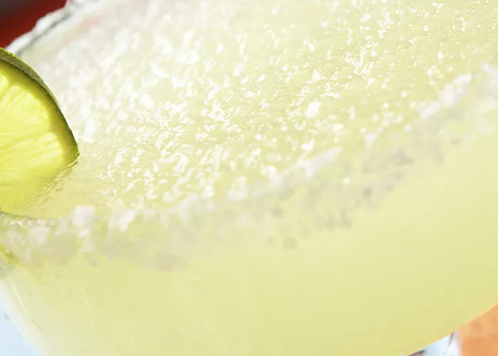 A coupe glass of Passion Fruit Passport garnished with  a  brandied or maraschino cherry.