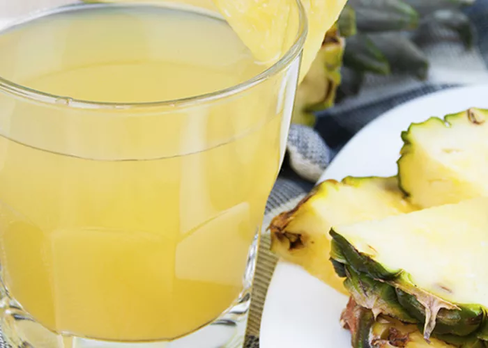 Glass of Pineapple Smash garnished with pineapple slice alongside some slices of pineapple