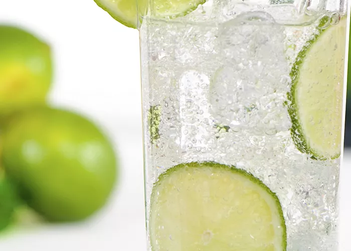 A glass of Cruzan® Summer Breeze with ice cube, topped with sparkling soda water, garnished with a lime wedge on the rim, and a straws.