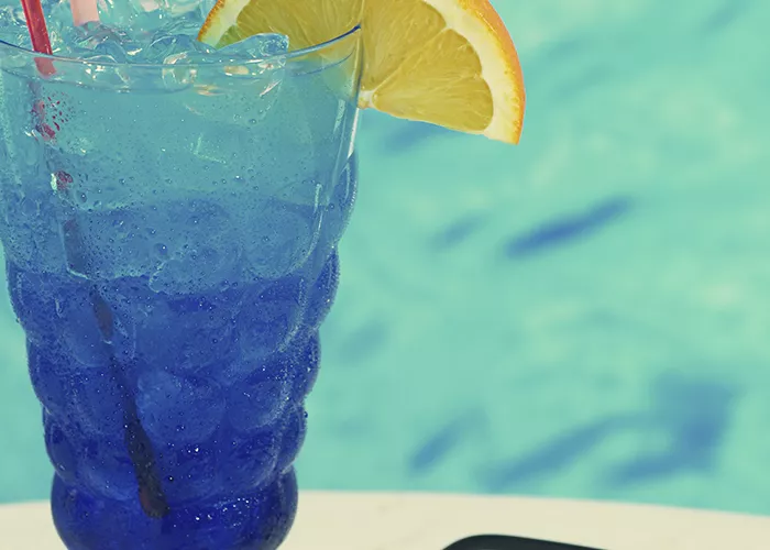 Glass of Blues on the Rocks with ice and a straws, garnished with a little umbrella, flamingo pick and a cherry and an orange slice on a pick