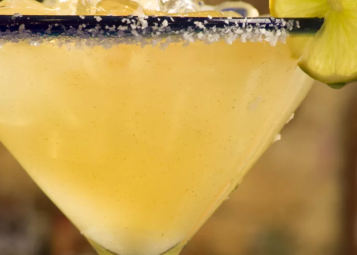 A glass of Nectarita, garnished with ice cubes, a wheel of lemon, and crushed sugar around the rim of the glass