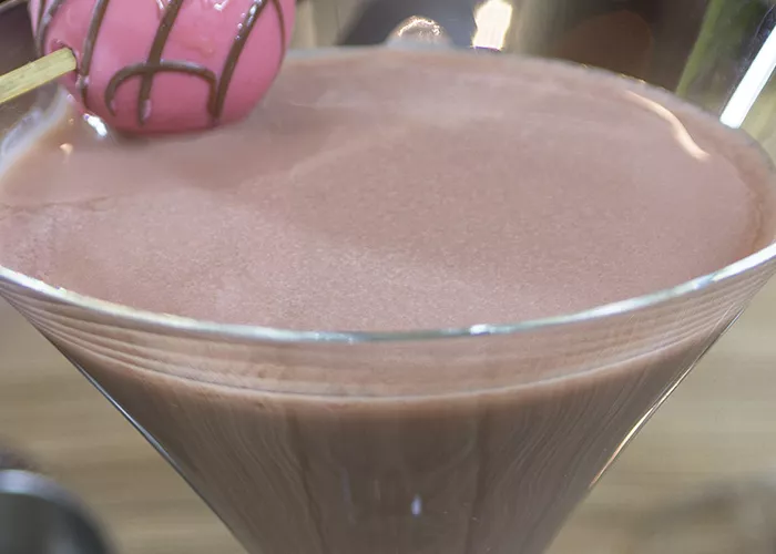 A glass of Razzmatazz® Truffle Martini garnished with a chocolate ball pierced on a cocktail pick on the rim.