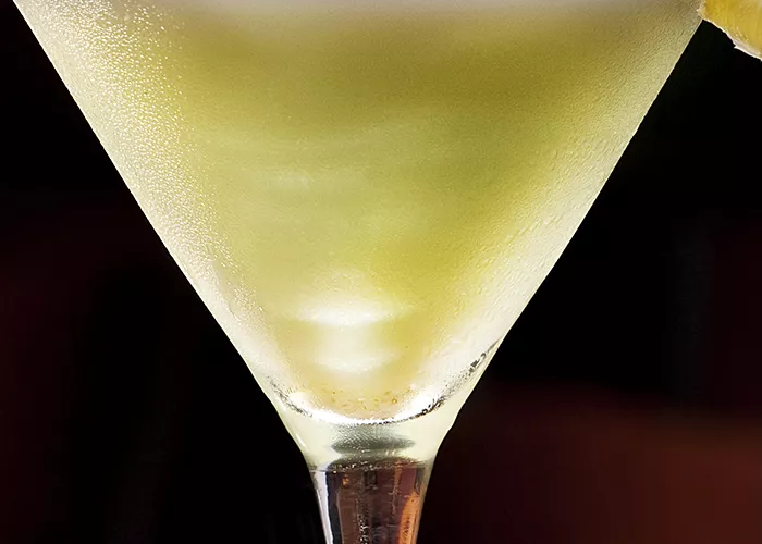 A glass of Sour Apple Popsicle Martini garnished with a slice of lime and crushed sugar on the rim