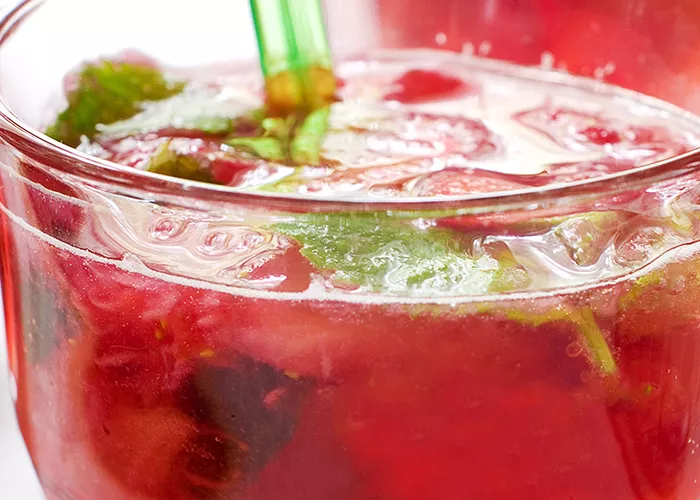 A glass of The Raspberry Julep garnished with Fresh Mint Leaves and fresh Raspberries and  a straws