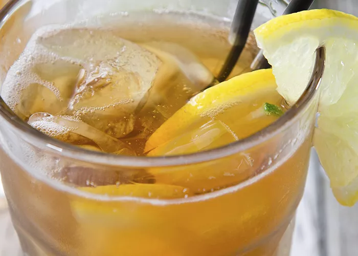 A glass of Fire Drop with crushed ice, lemon peels, and 2 black straws inside. Garnished with a lemon peel on the glass