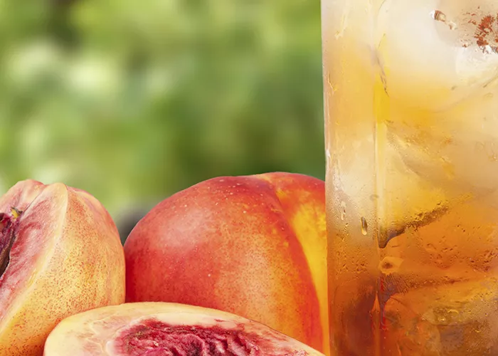 A glass of Front Porch Peach Tea with a peach and half a peach on the side, refreshing and fruity.