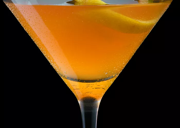 Glass of Citrus Basil Manhattan garnished with a lemon twist and basil leaves.