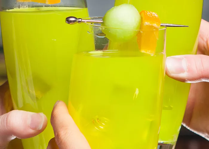 Three person cheersing with glass of Fuzzy Melon Ball garnished with orange slice and melon ball