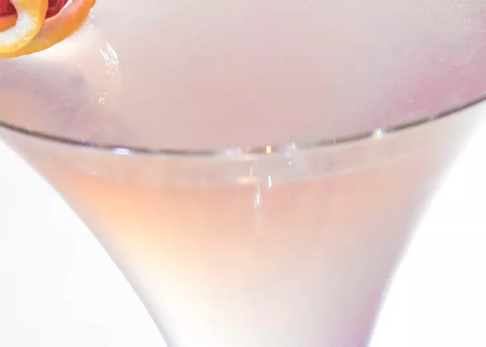 A martini glass of Chocolate Covered Berries, garnished with a stick featuring a lemon peel and raspberry.