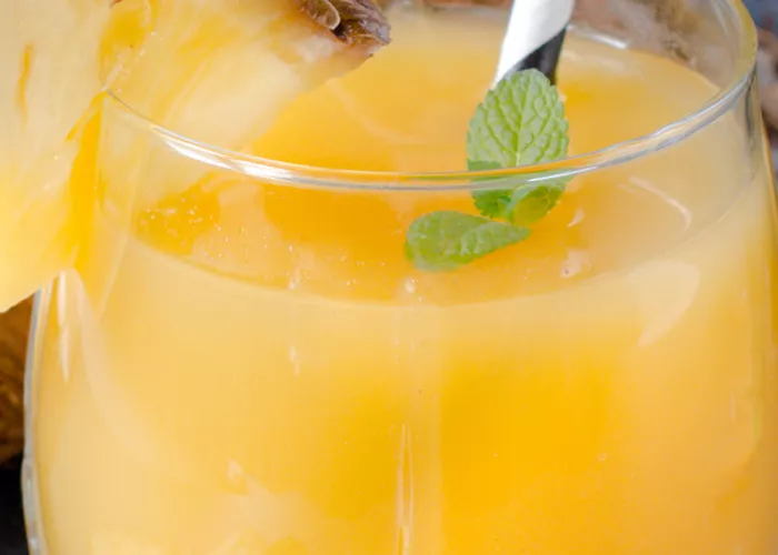 A glass of Coconut Spritzer, garnished with a pineapple slice, mint leaves and straws.