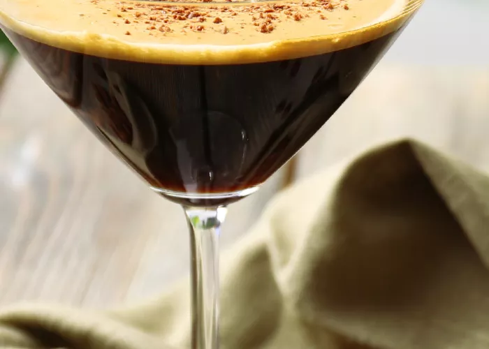 A cocktail glass of Mocha Razz-Tini garnished with powdered chocolate, alongside a napkin, placed with some powdered chocolate spread nearby.
